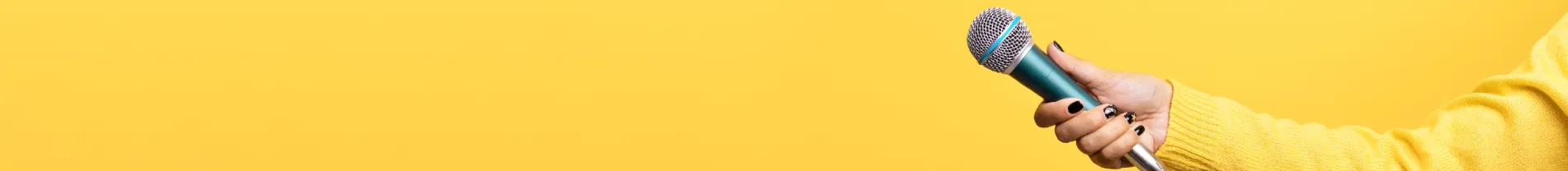 Ruka v žlutém svetru držící mikrofon proti žlutému pozadí.